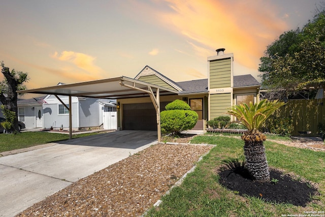 view of front facade featuring fence, an attached garage, a chimney, concrete driveway, and an attached carport