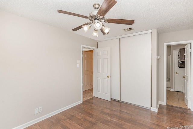 unfurnished bedroom with a closet, baseboards, a textured ceiling, visible vents, and wood finished floors