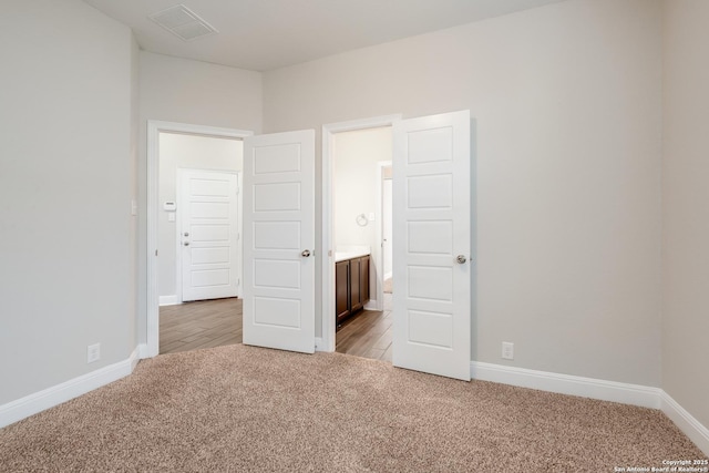 unfurnished bedroom with light carpet, visible vents, baseboards, and connected bathroom