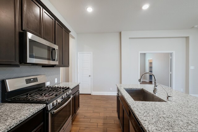 kitchen featuring appliances with stainless steel finishes, light stone counters, a sink, decorative backsplash, and dark wood-style floors