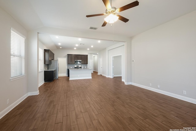 unfurnished living room with dark wood-style floors, baseboards, a ceiling fan, and visible vents