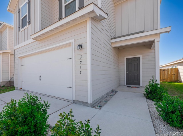 view of exterior entry with board and batten siding, an attached garage, fence, and concrete driveway