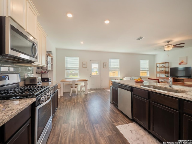 kitchen with ceiling fan, light stone countertops, appliances with stainless steel finishes, a sink, and dark wood-style floors