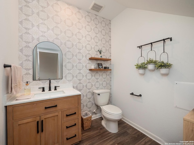 half bathroom featuring vanity, visible vents, toilet, wood finished floors, and baseboards