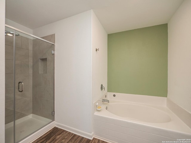 bathroom featuring baseboards, a stall shower, wood finished floors, and a garden tub