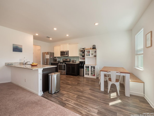 kitchen with baseboards, light stone counters, a peninsula, white cabinetry, and stainless steel appliances