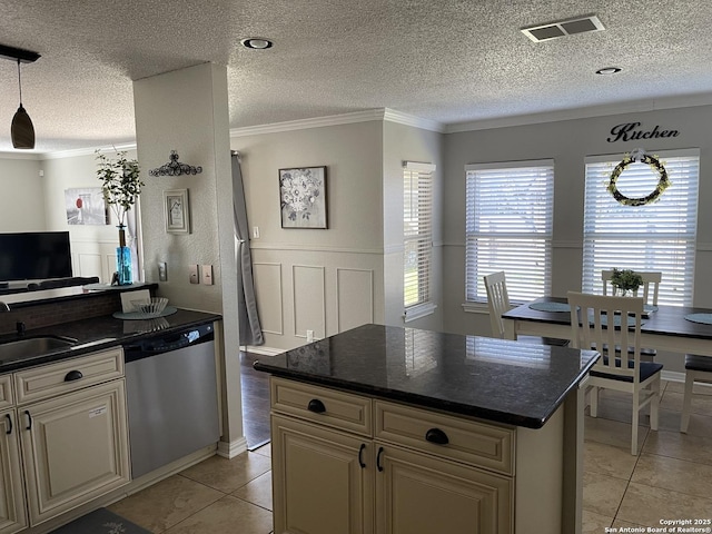 kitchen featuring light tile patterned floors, cream cabinetry, dark countertops, stainless steel dishwasher, and a sink