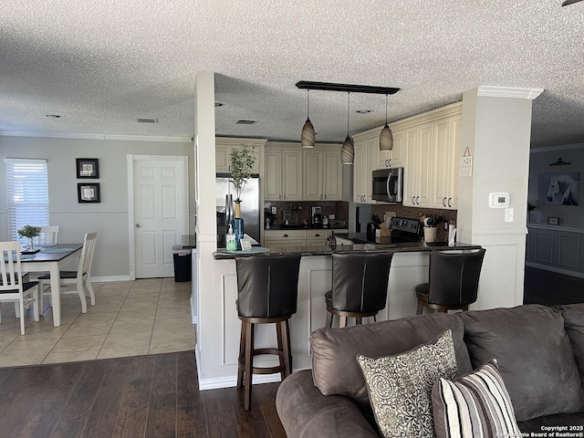 kitchen with ornamental molding, cream cabinetry, dark countertops, stainless steel appliances, and open floor plan