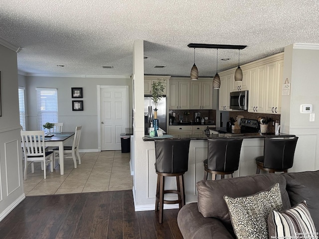 kitchen with open floor plan, cream cabinetry, dark countertops, stainless steel appliances, and wood finished floors