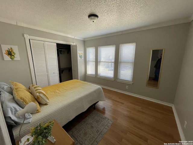 bedroom with a closet, a textured ceiling, baseboards, and wood finished floors