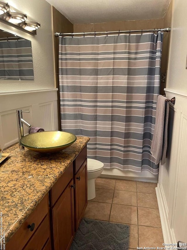 bathroom featuring a decorative wall, toilet, a wainscoted wall, vanity, and tile patterned floors