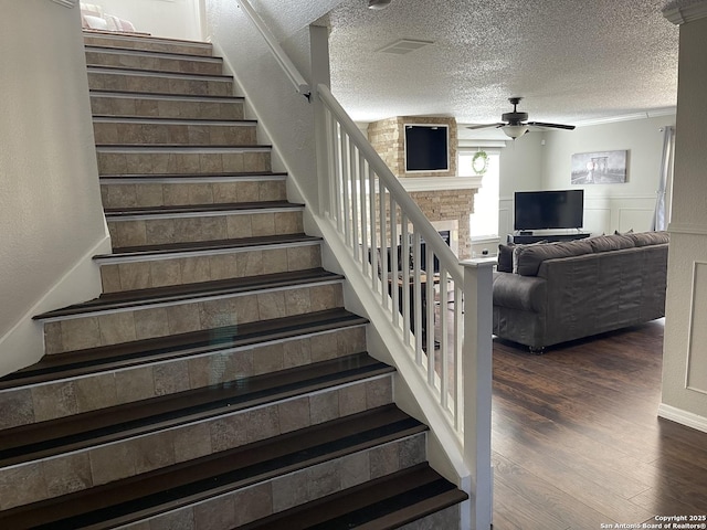 stairs with a brick fireplace, a textured ceiling, a ceiling fan, and wood finished floors