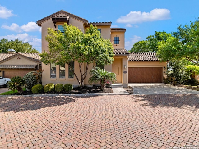 mediterranean / spanish house featuring stucco siding, decorative driveway, an attached garage, and a tile roof