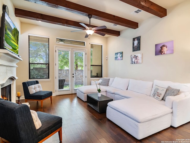 living area featuring a warm lit fireplace, visible vents, beam ceiling, dark wood finished floors, and ceiling fan