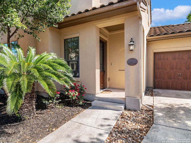 doorway to property featuring stucco siding, an attached garage, and a tile roof