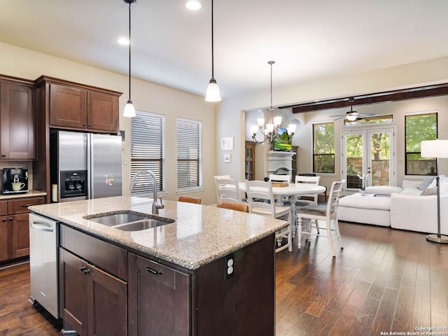 kitchen featuring ceiling fan with notable chandelier, dark wood-style flooring, a sink, stainless steel appliances, and a center island with sink