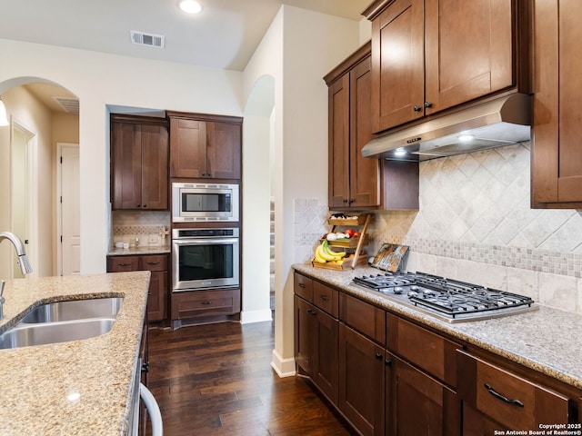 kitchen with arched walkways, visible vents, under cabinet range hood, a sink, and stainless steel appliances