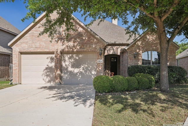 view of front of property featuring an attached garage, a shingled roof, concrete driveway, and brick siding