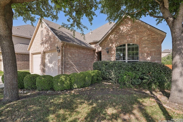 view of front of home with brick siding, an attached garage, and a shingled roof