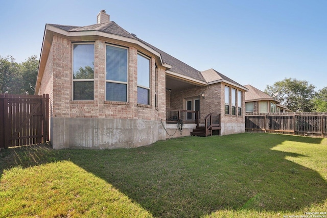 rear view of house with brick siding, a fenced backyard, a chimney, and a lawn