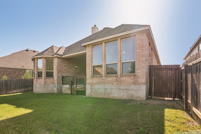 rear view of property featuring a fenced backyard, a lawn, brick siding, a chimney, and a shingled roof