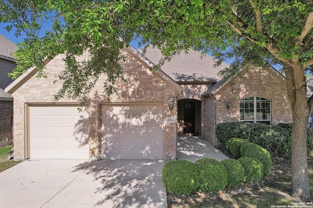 view of front of home with concrete driveway, roof with shingles, brick siding, and an attached garage