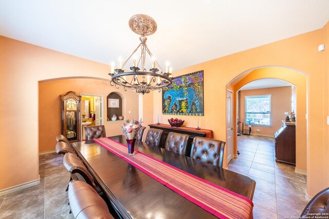dining room with tile patterned floors, arched walkways, an inviting chandelier, and baseboards