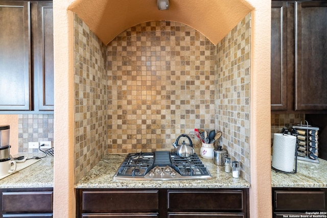 kitchen with tasteful backsplash, dark brown cabinets, vaulted ceiling, stainless steel gas cooktop, and light stone counters