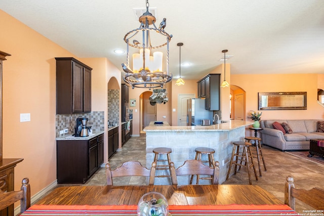 kitchen featuring dark brown cabinets, freestanding refrigerator, arched walkways, and light stone counters