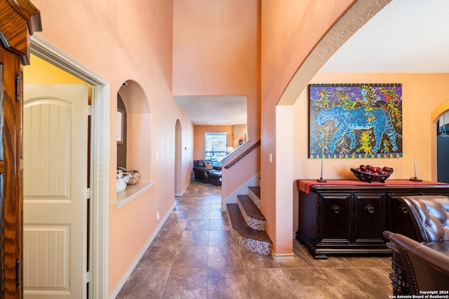 corridor with arched walkways, a towering ceiling, baseboards, and stairway