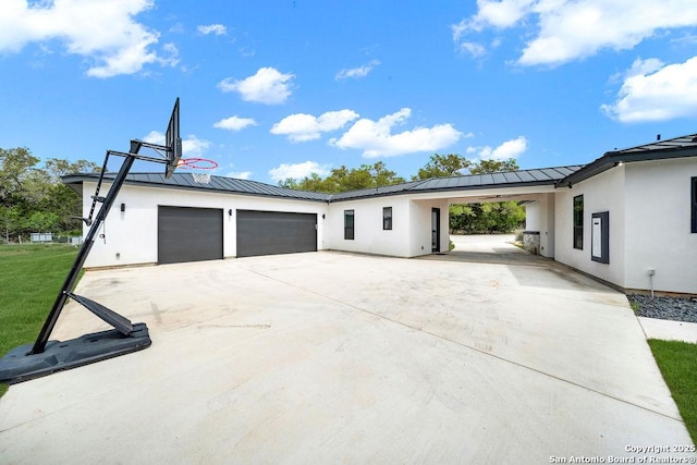 exterior space with a standing seam roof, stucco siding, metal roof, an attached garage, and driveway