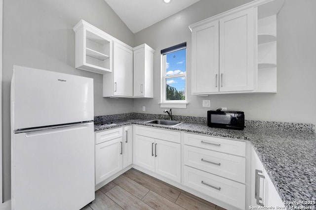 kitchen with open shelves, a sink, freestanding refrigerator, black microwave, and white cabinetry
