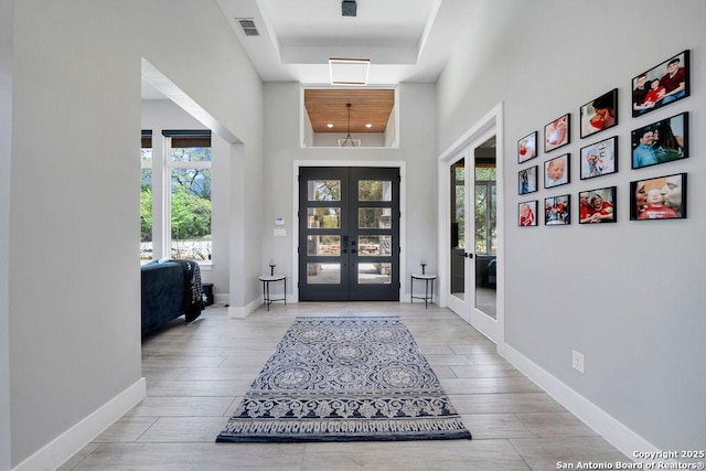 foyer featuring a towering ceiling, visible vents, wood finished floors, a raised ceiling, and french doors