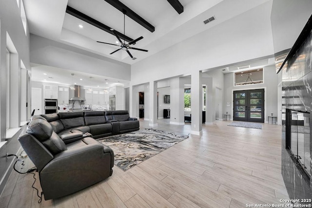living room featuring french doors, a high ceiling, visible vents, beamed ceiling, and light wood finished floors