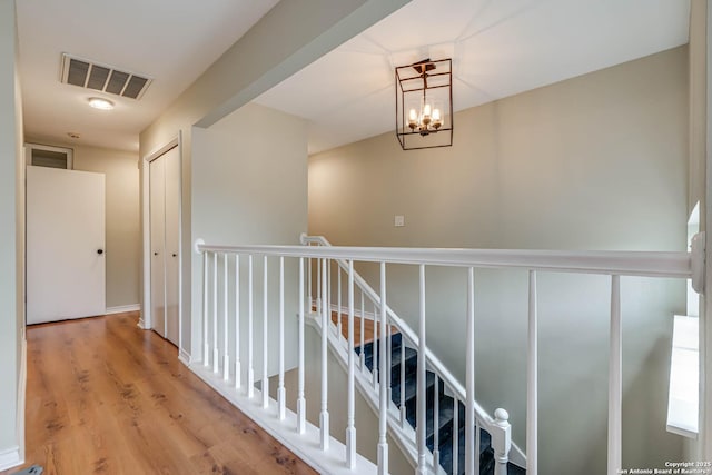hall with visible vents, an upstairs landing, a notable chandelier, and wood finished floors