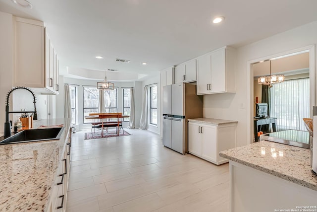 kitchen with freestanding refrigerator, white cabinets, visible vents, a chandelier, and a sink