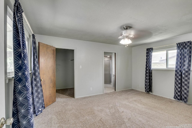 unfurnished bedroom featuring baseboards, a spacious closet, a textured ceiling, connected bathroom, and carpet flooring