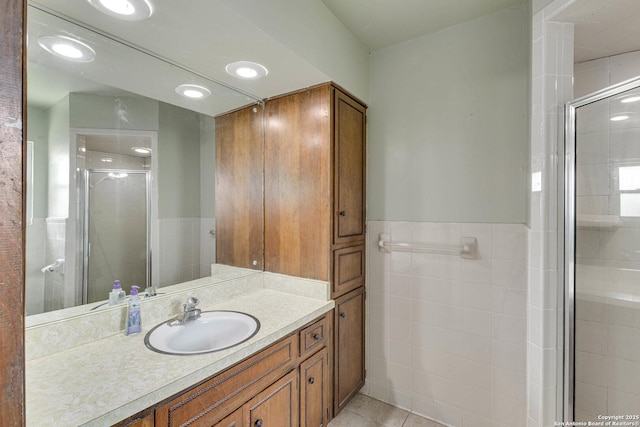 bathroom featuring vanity, a stall shower, tile patterned floors, wainscoting, and tile walls