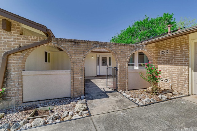 entrance to property featuring brick siding, fence, and a gate
