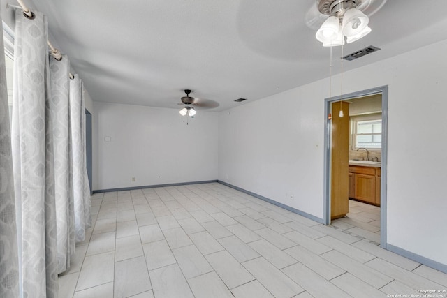 unfurnished room with a sink, ceiling fan, baseboards, and visible vents