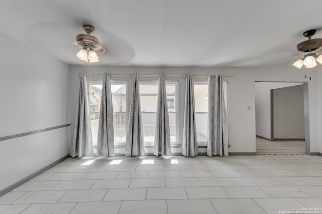empty room featuring ceiling fan, plenty of natural light, and baseboards