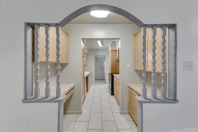 hall featuring arched walkways, baseboards, and light tile patterned flooring