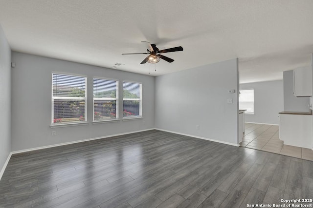unfurnished living room with dark wood-type flooring, baseboards, a ceiling fan, and visible vents