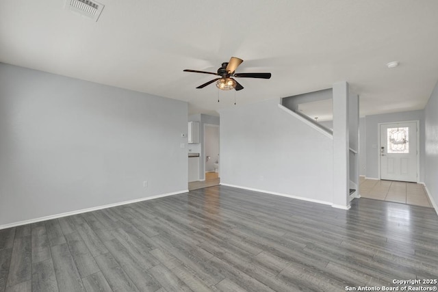 unfurnished living room featuring visible vents, baseboards, ceiling fan, wood finished floors, and stairs