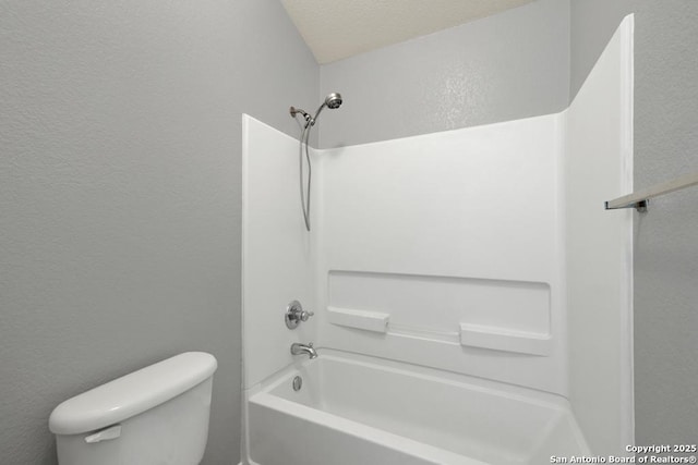 bathroom featuring a textured wall, bathing tub / shower combination, and toilet