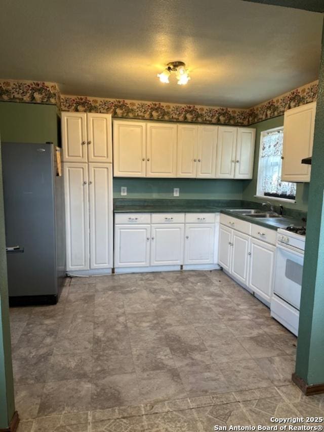 726 Southcross, San Antonio, TX 78211 - kitchen featuring dark countertops, a sink, white gas range, freestanding refrigerator, and white cabinetry