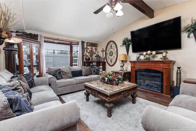 living room featuring ceiling fan, vaulted ceiling with beams, a glass covered fireplace, and wood finished floors