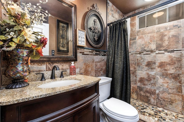full bath with a tile shower, tile walls, vanity, and toilet