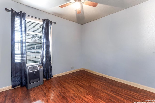 unfurnished room featuring ceiling fan, heating unit, baseboards, and dark wood finished floors