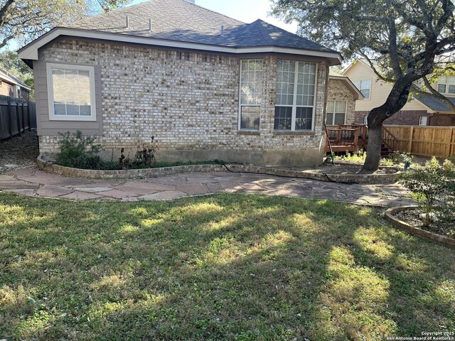 view of home's exterior featuring a deck, roof with shingles, fence, a yard, and brick siding
